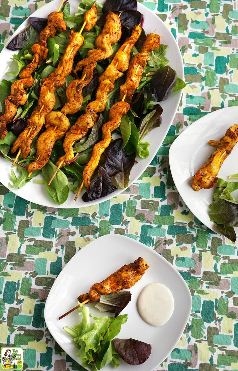 Plates of Chicken Shawarma Appetizers on Skewers with Dipping Sauce served on beds of lettuce.