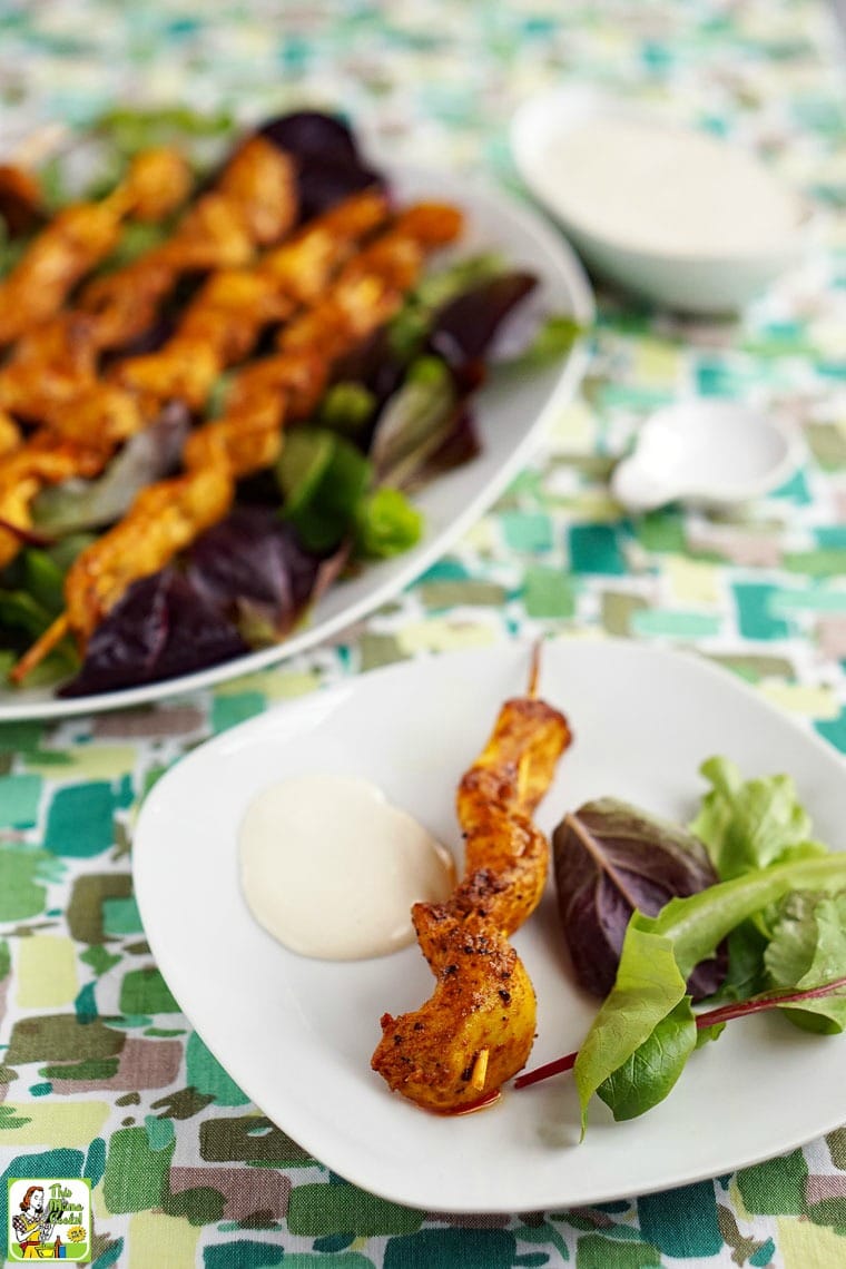 Plates of Chicken Shawarma Appetizers on Skewers with Dipping Sauce served on beds of lettuce.