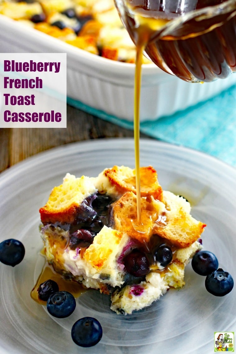 A piece of Blueberry French Toast Casserole in a white plate with maple syrup being poured from a small glass pitcher.