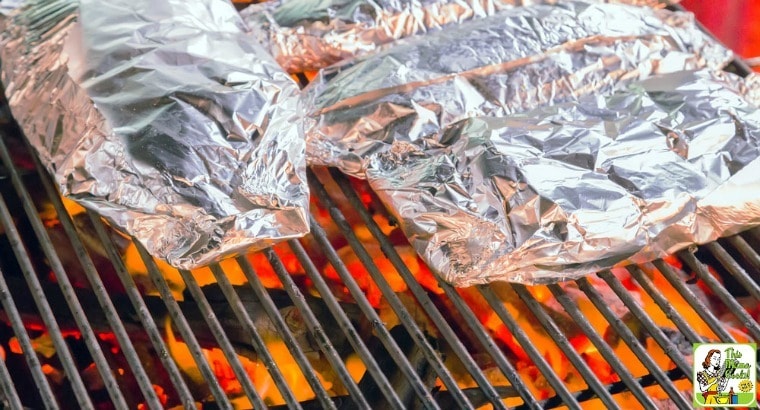 Packets of grilled salmon in foil on a grate over a campfire.