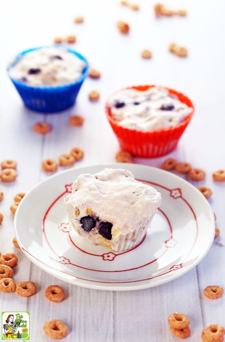 Frozen yogurt bites in silicon baking cups and on a plate with cheerios on a tabletop.