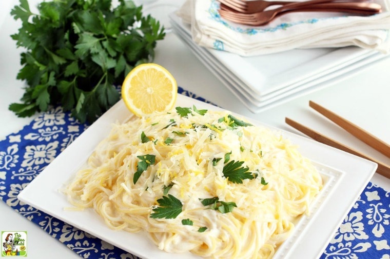 Simple Lemon Pasta on a white plate on a blue placemate with plate, napkins, forks, and a bunch of parsley.