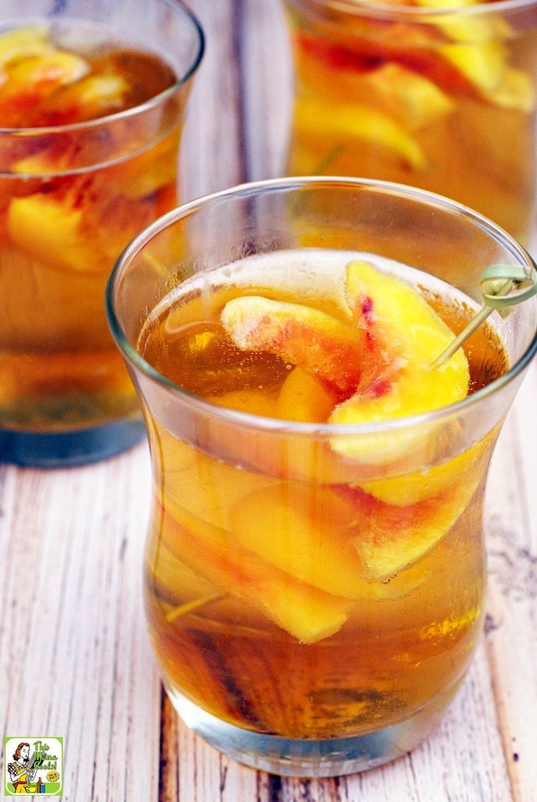 Closeup of 3 glasses of Peach Whiskey Cocktails with slices of peaches on bamboo skewers.