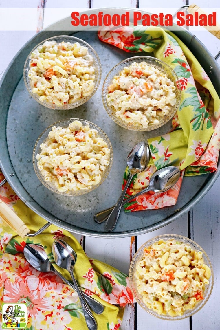 Overhead view of bowls of Seafood Pasta Salad on a metal tray with floral napkins and spoons.