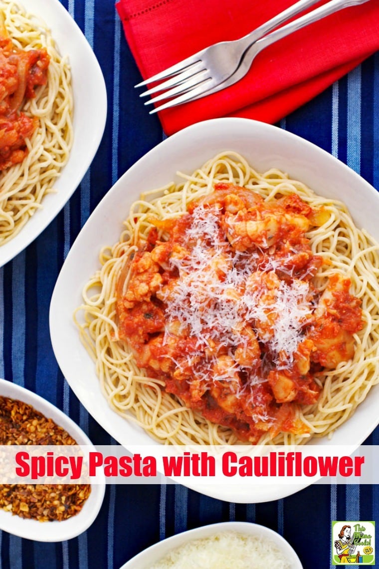 Spicy Pasta with Cauliflower in a white bowl on a blue striped tablecloth with bowls of shredded cheese and chili pepper flakes.