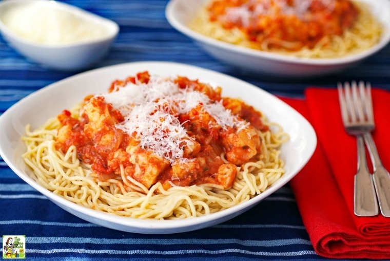 White bowl of spaghetti with cauliflower in sauce with a red napkin and two forks.