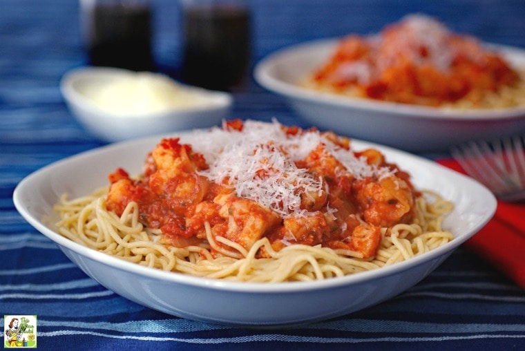 A bowl of pasta cauliflower sauce with bowl of shredded cheese and pasta in the background.