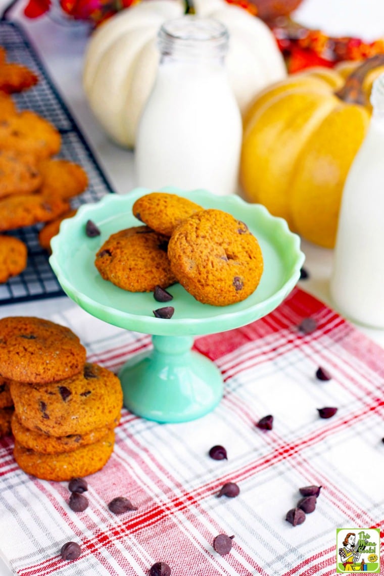 Stacks of pumpkin chocolate chip cookies on a green cake stand and a red and white napkin.