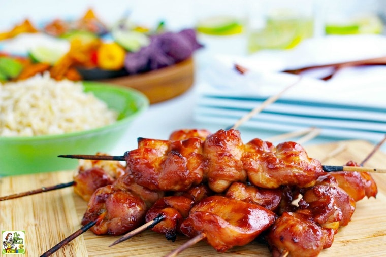 Sriracha Chicken Kabobs on a wooden platter with a bowl of rice and plates in the background.