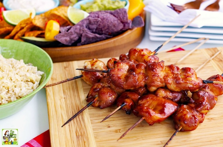 Chicken kabobs skewers, bowl of rice, and chips and guacamole.