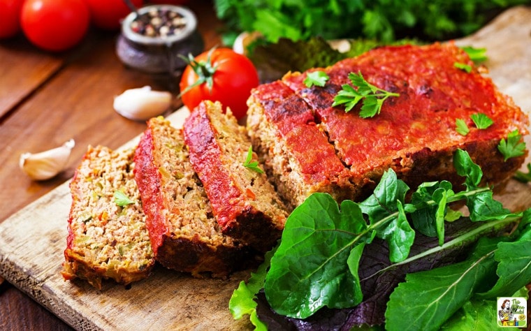 Smoked Meatloaf on a wooden cutting board with herbs, tomatoes, garlic, and seasonings.