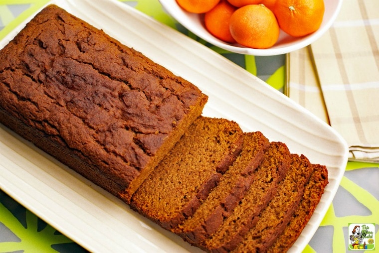 Overhead shot of a Pumpkin Bread sliced up on a white plate with a bowl of tangerines.