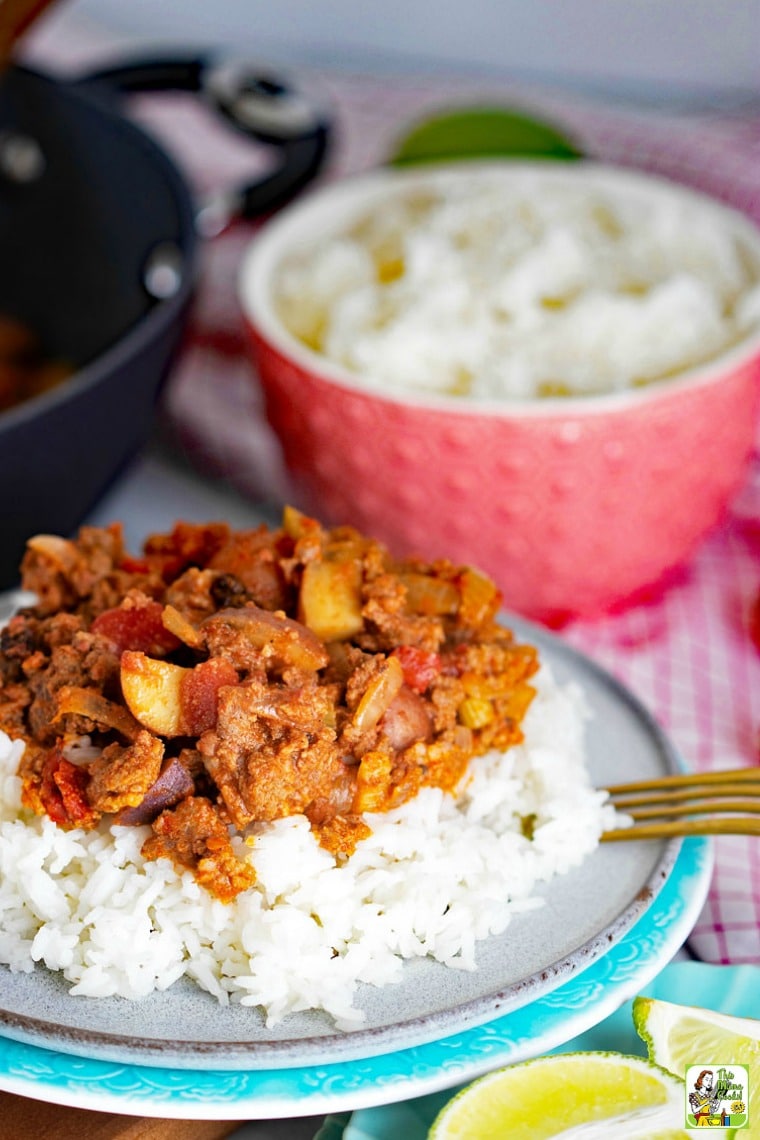 Plate of Mexican Picadillo on rice with brass fork with a pink bowl of rice and saute plan in the background.