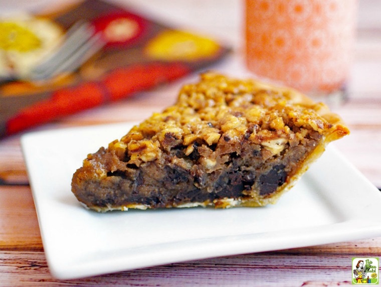 A slice of Gluten Free Chocolate Pecan Pie on a white plate with fork, napkin and glass of milk in the background.