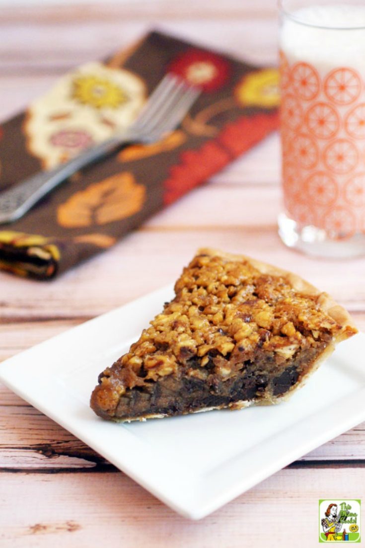 A slice of chocolate gluten free pecan pie on a square white plate with a glass of milk and napkin in the background.