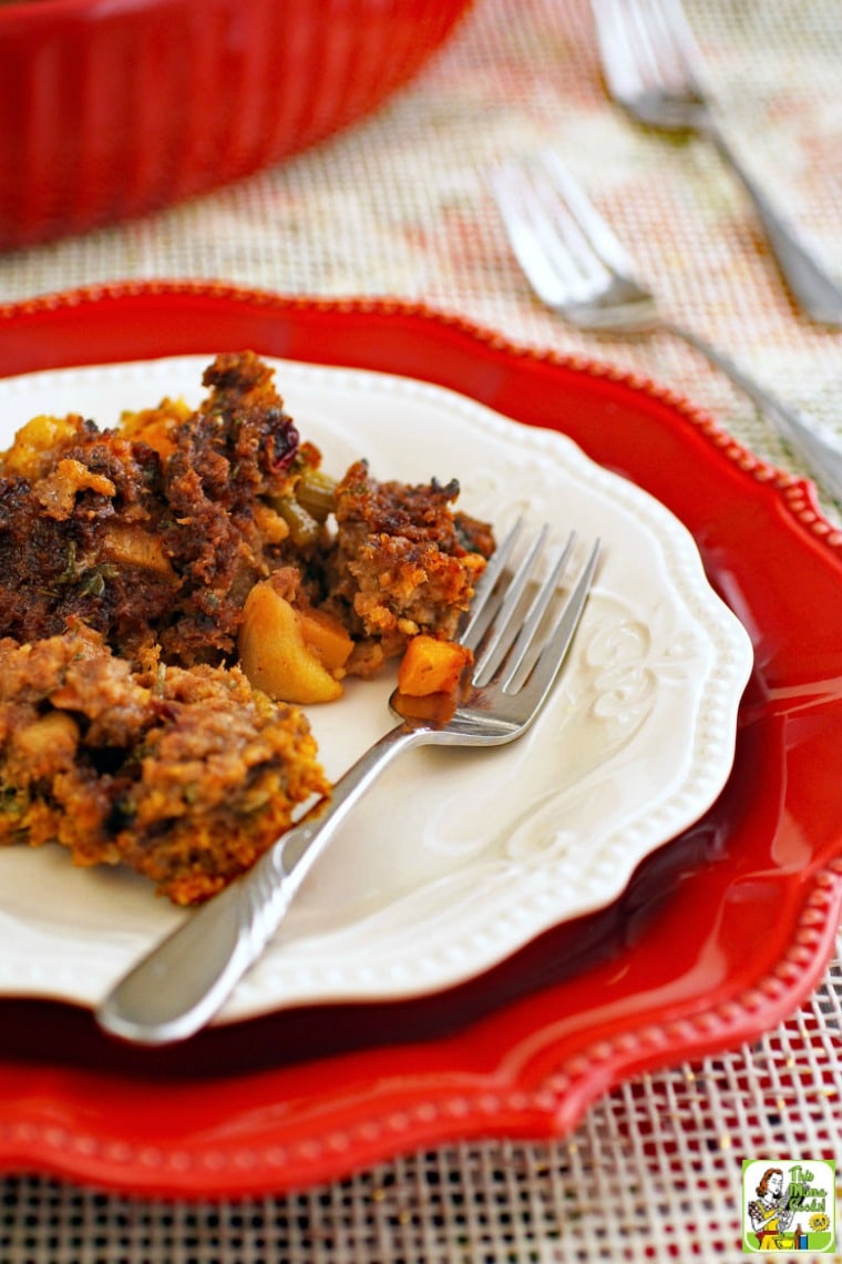 A plate of gluten free stuffing with fork on a larger red plate with casserole dish and serving forks in the background.