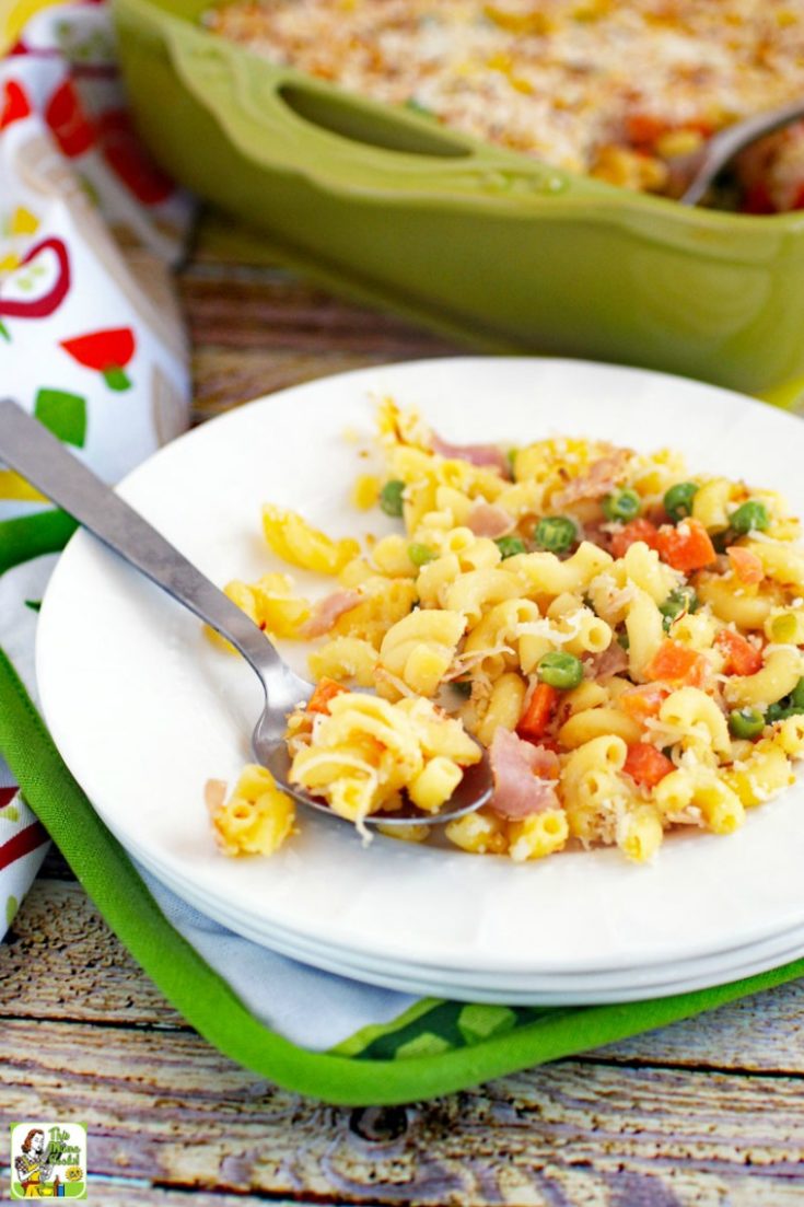 A white plate of mac and cheese with peas, carrots & ham