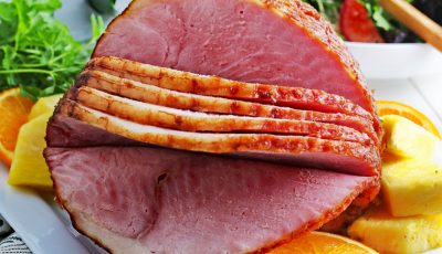 Closeup of crockpot spiral ham on a plate with slices of oranges and pineapple.