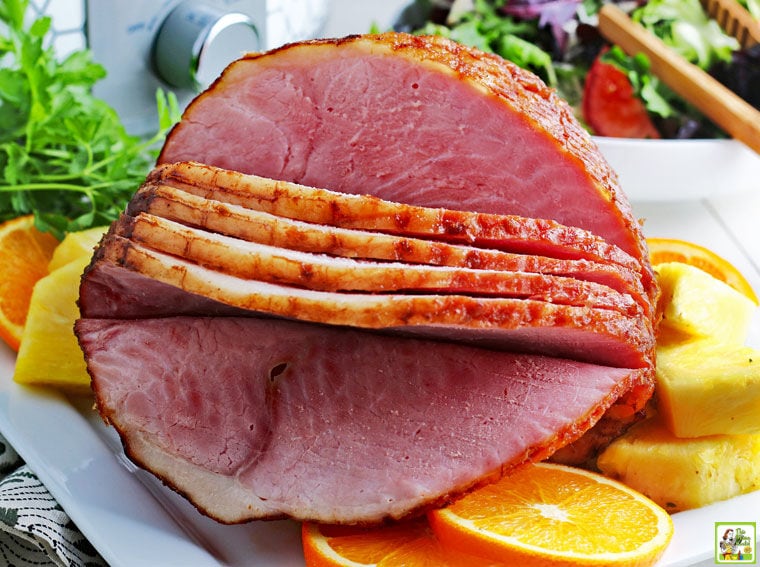 Closeup of crockpot spiral ham on a plate with slices of oranges and pineapple.