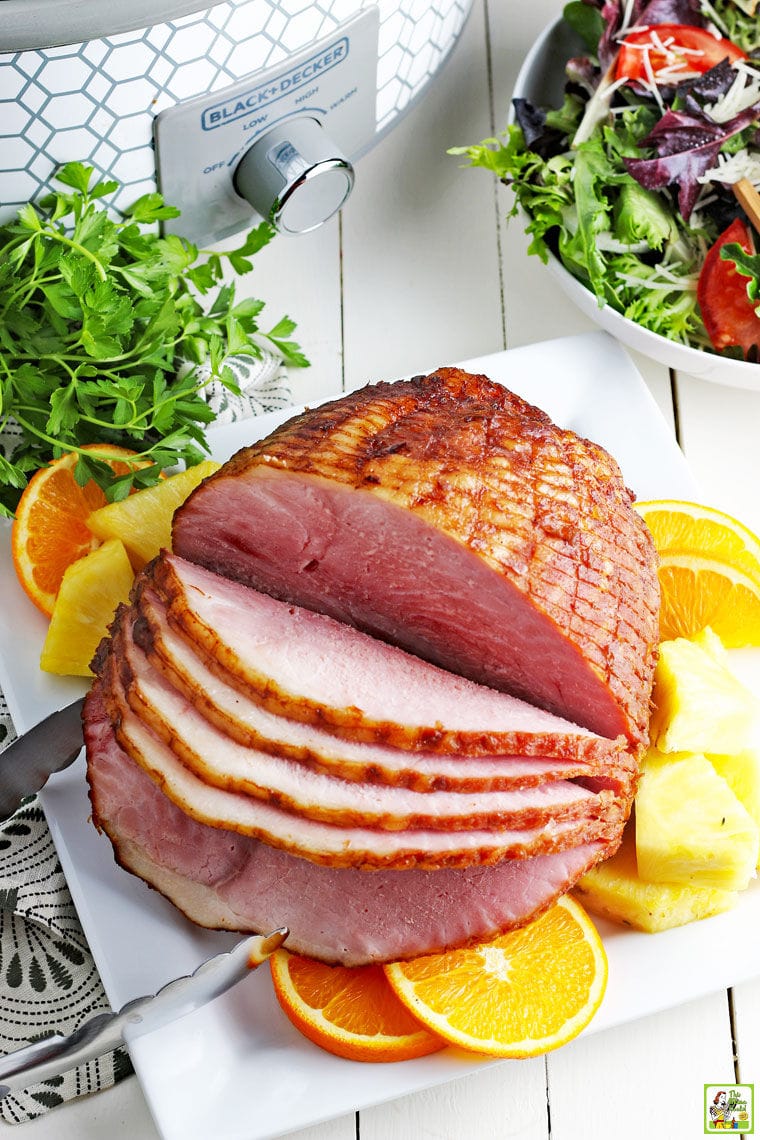 Overhead shot of a crockpot spiral ham on a plate with a bowl of lettuce and a slow cooker in the background.