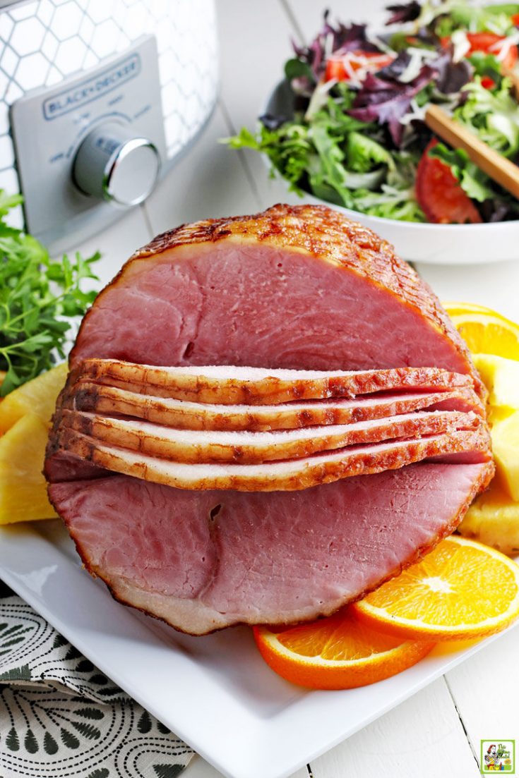 Slow cooker sliced ham on a plate with a bowl of lettuce and a crock pot in the background.