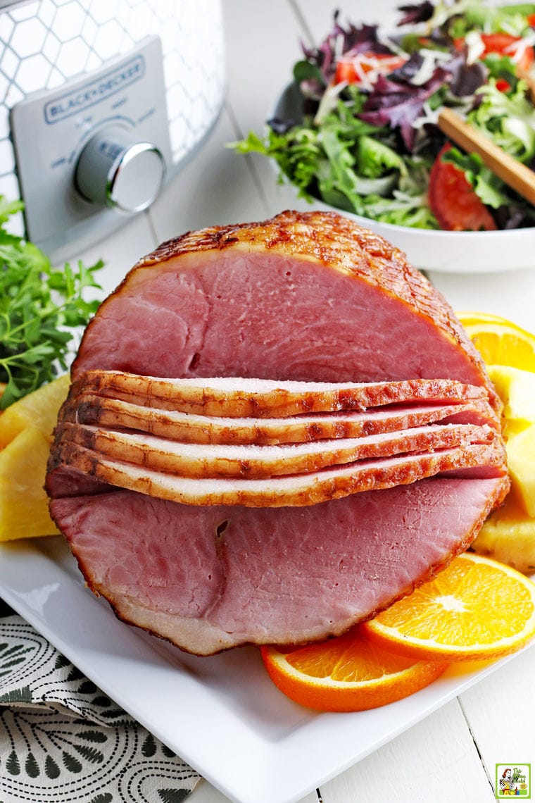 Slow cooker sliced ham on a plate with a bowl of lettuce and a crock pot in the background.