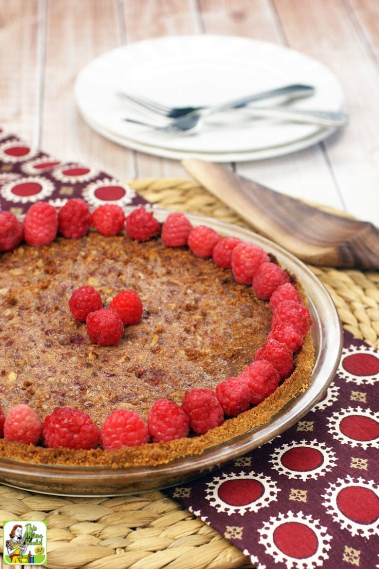 Gluten free pecan pie with raspberries, plates, forks, and pie server.