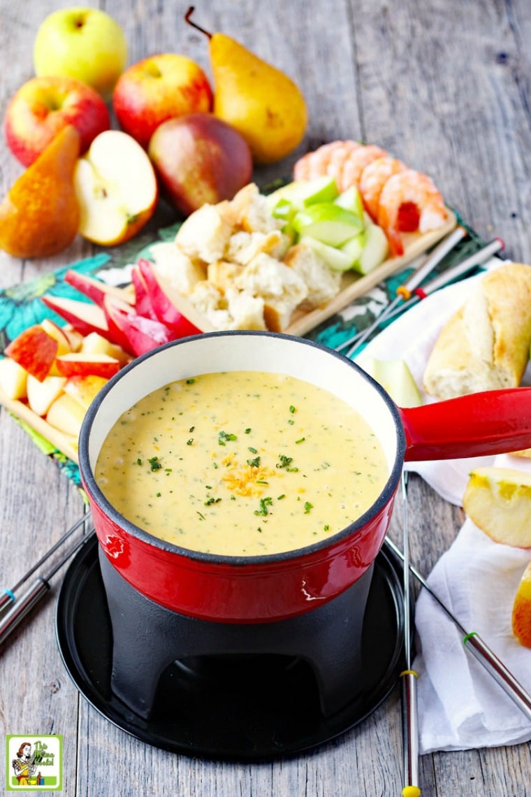 A pot of brie fondue and fondue forks with dipping foods on trays in the background.