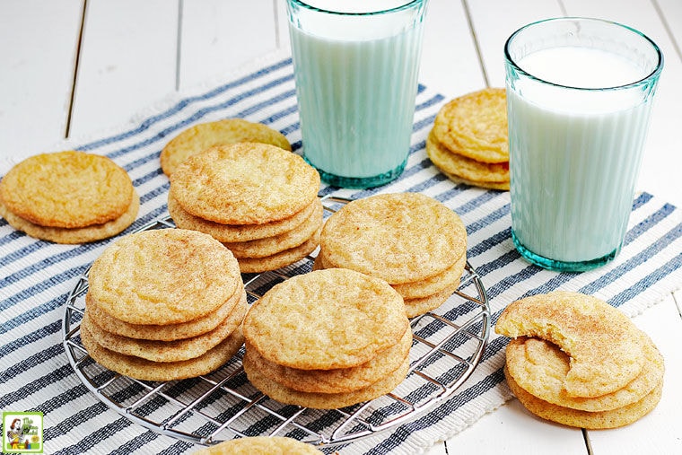 Stacks of Rice Flour Snickerdoodles Cookies on a wire rack and striped napkin with glasses of milk.