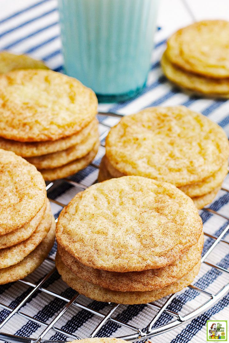 Stacks of rice flour snickerdoodles cookies on a striped napkin with a glass of milk.