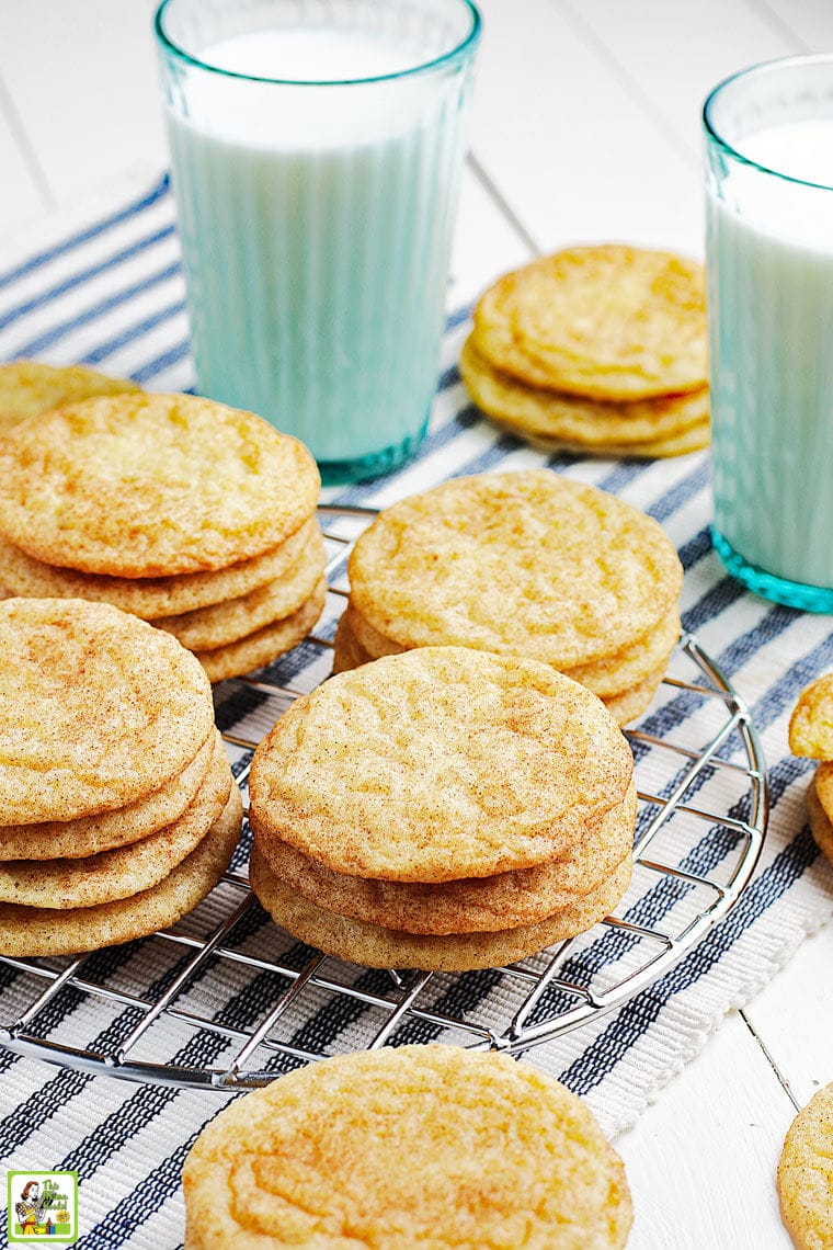 Gluten free snickerdoodles cookies on a wire rack on a striped napkin with glasses of milk.