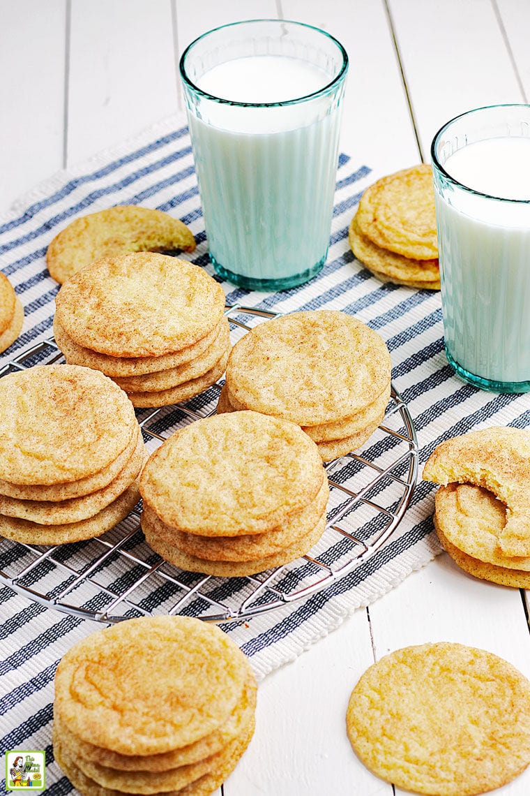 Stacks of snickerdoodles cookies on a striped napkin with glasses of milk.