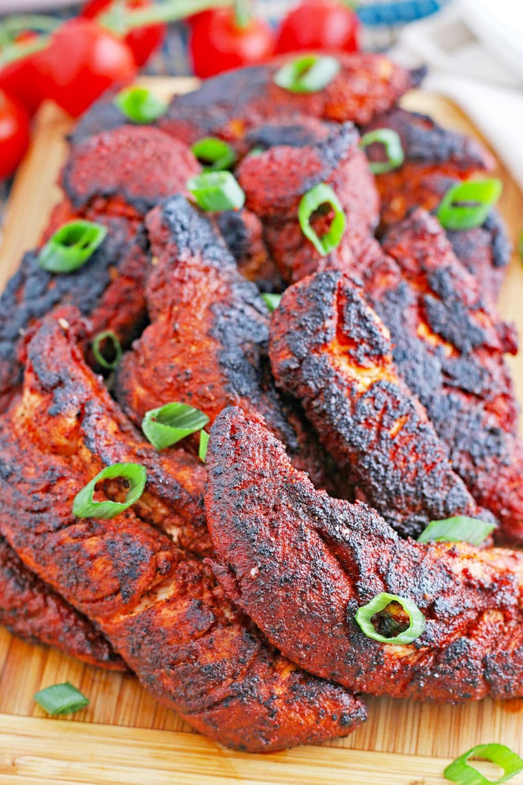 A pile of blackened chicken tenders on a wooden cutting board.