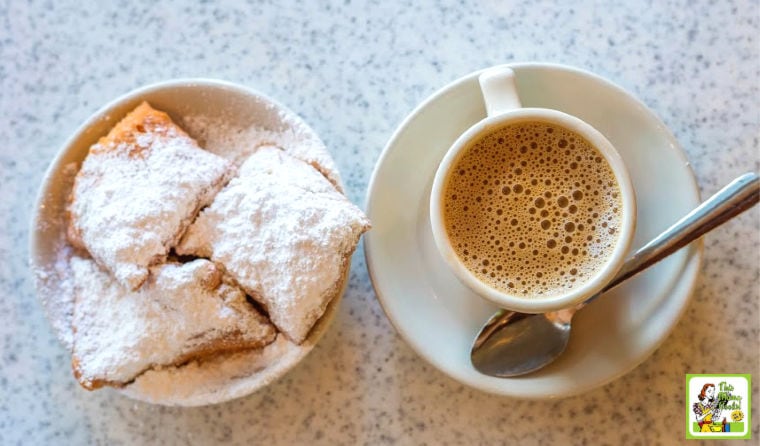 French style donuts also called beignets topped with powdered sugar next to a cup of frothy coffee.