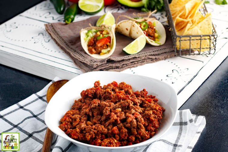 A bowl of Crockpot Taco Meat with wooden serving spoon, napkin, and tacos, tortilla chips, and limes in the background.