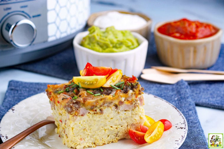 A slice of Crockpot Breakfast Casserole on a plate with bowls of toppings and a slow cooker in the background.