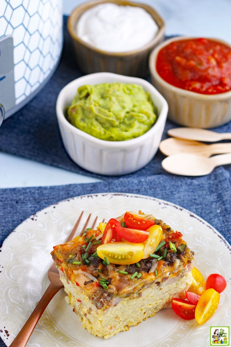 A plate of Crockpot Breakfast Casserole with tomatoes. Bowls of guacamole, sour cream, salsa in the background.