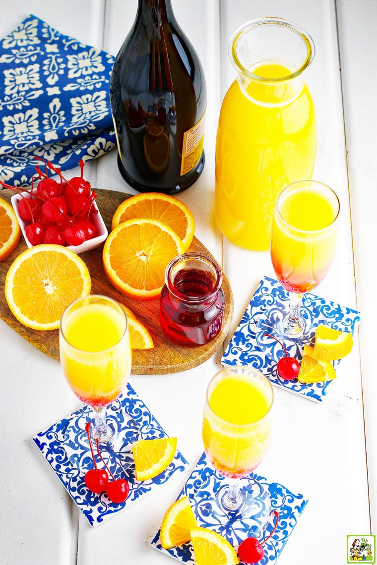 Prosecco Mimosas in champagne glasses, garnished with maraschino cherries and orange slices.