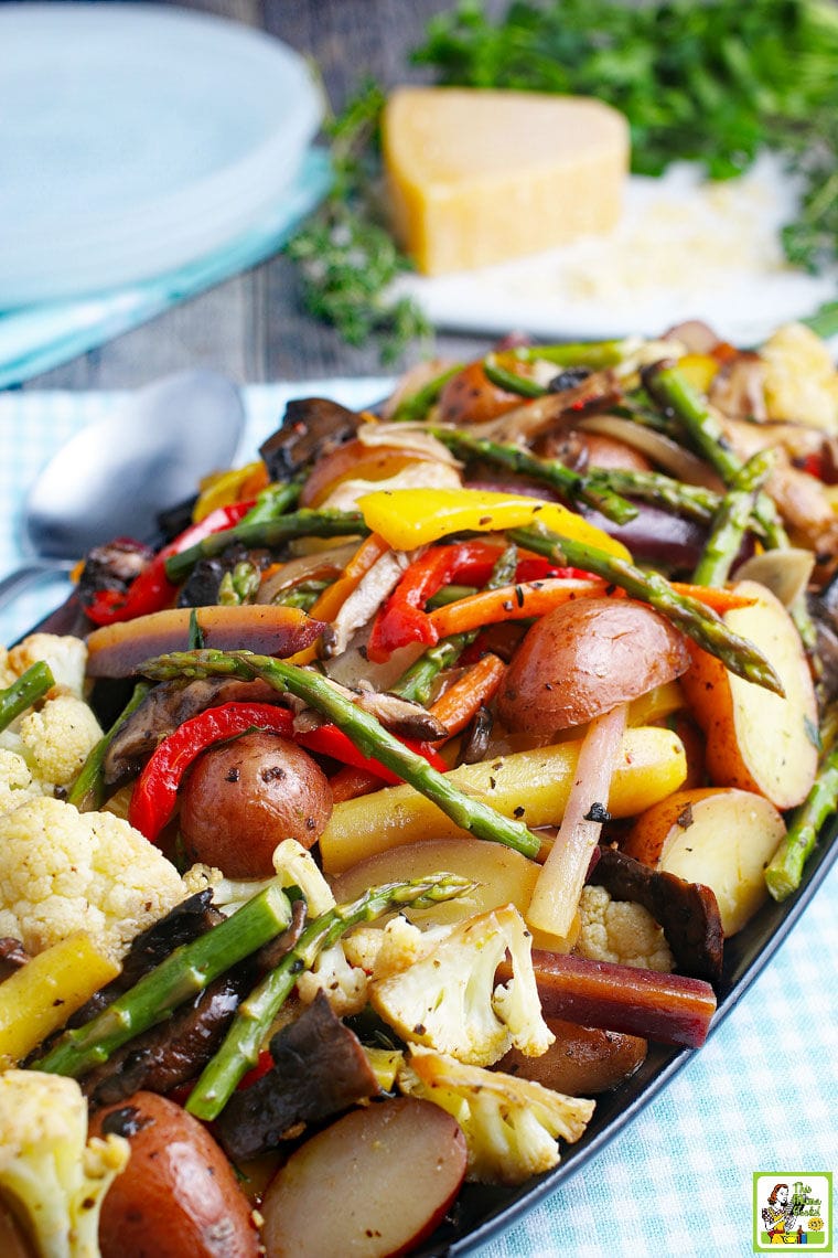 Closeup of a platter of roasted vegetables with a wedge of cheese in the background.