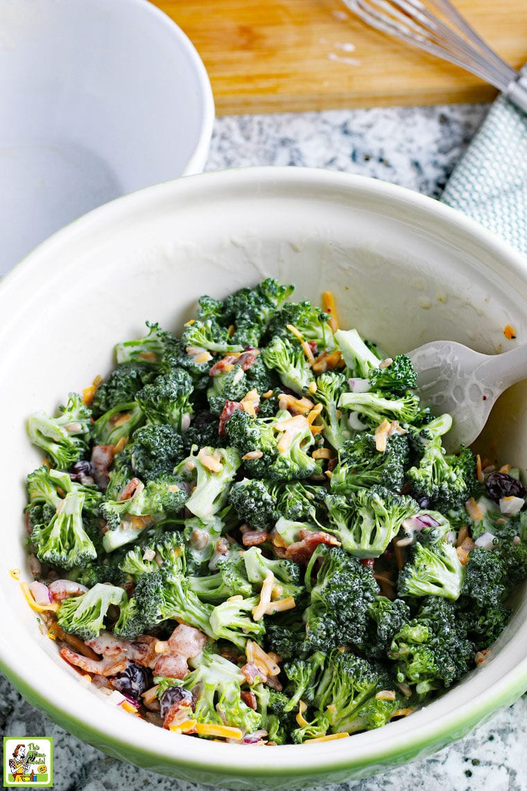 White bowl of Broccoli Bacon Salad with red onions and shredded cheddar cheese.
