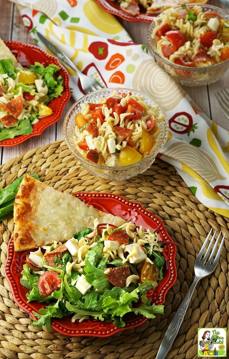 Plates and bowls of Caprese Pasta Salad with napkins and forks.