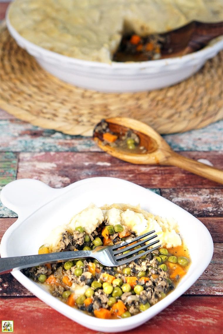 A plate of shepherd's pie with ground turkey with a platter of shepherd's pie and a wooden spoon in the background.