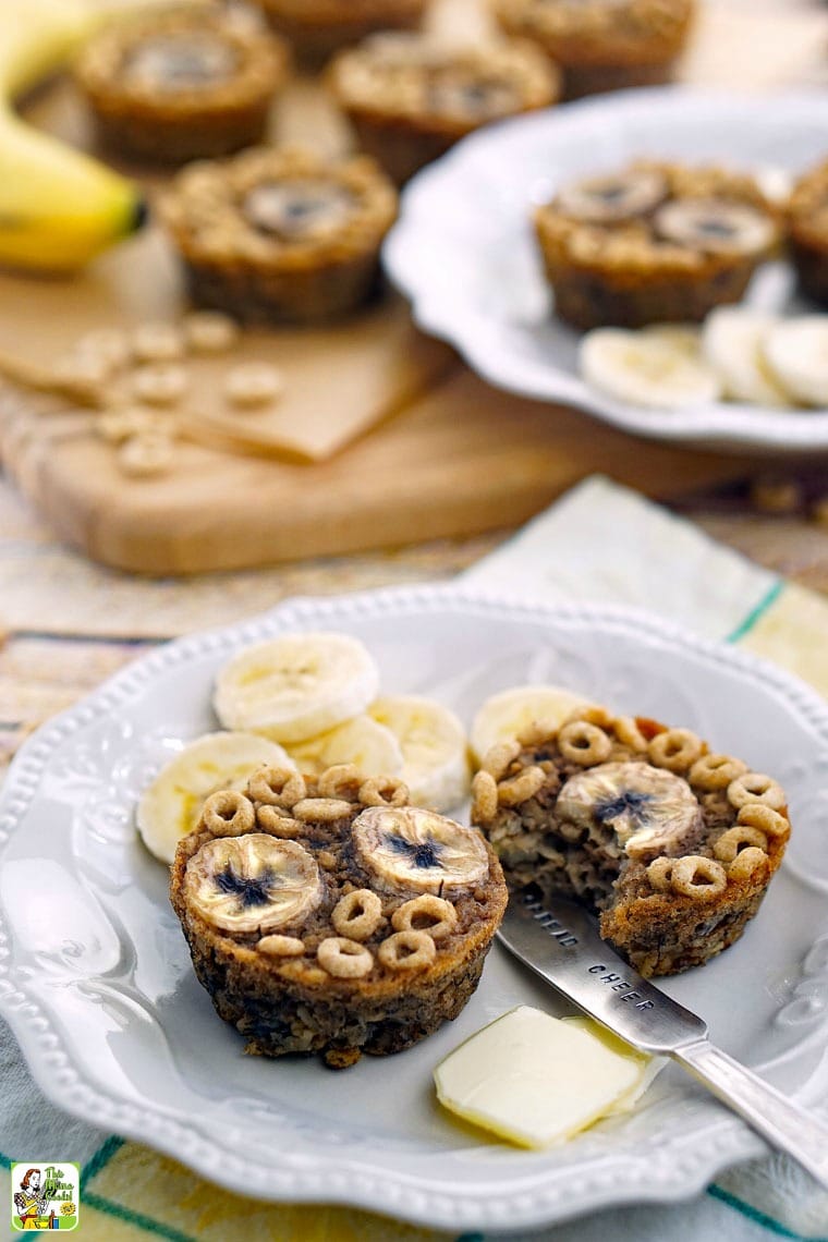 Two gluten free banana muffins on a white plate with slices of banana and butter pats.