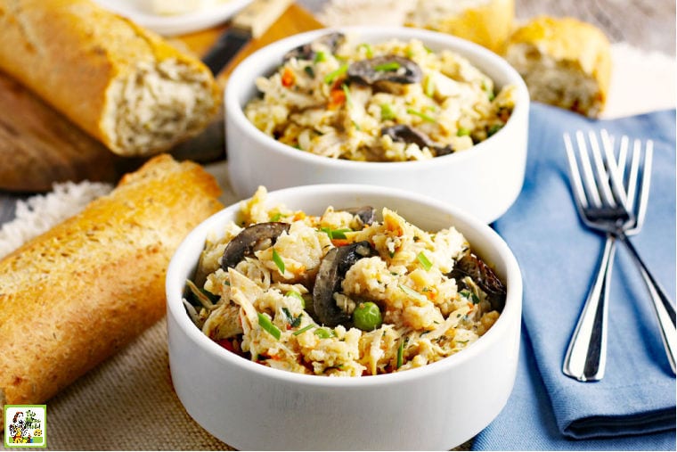 Two white bowls of Instant Pot Chicken and Rice with forks, blue napkins, and pieces of French bread.