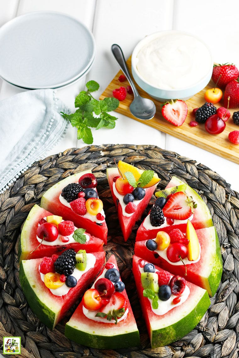 A Watermelon Pizza with cream cheese frosting, fruit and plates
