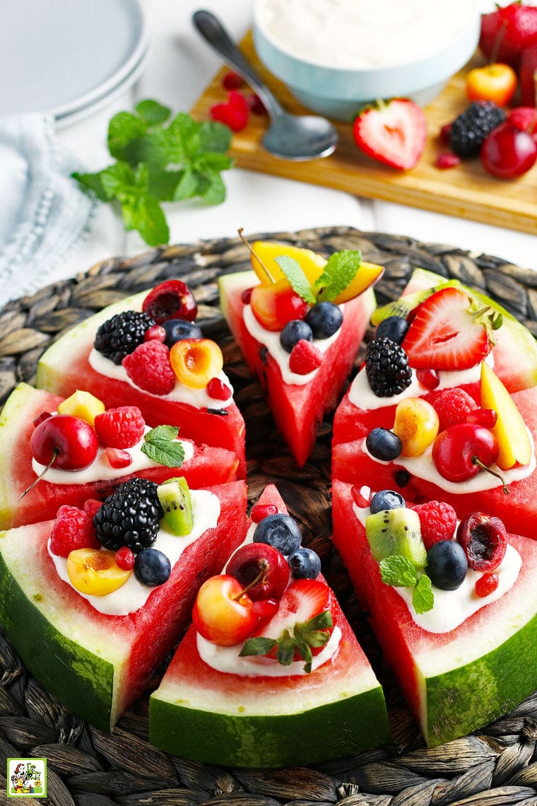 Slices of watermelon pizza with fruit and mint on a woven straw mat on a white tablecloth