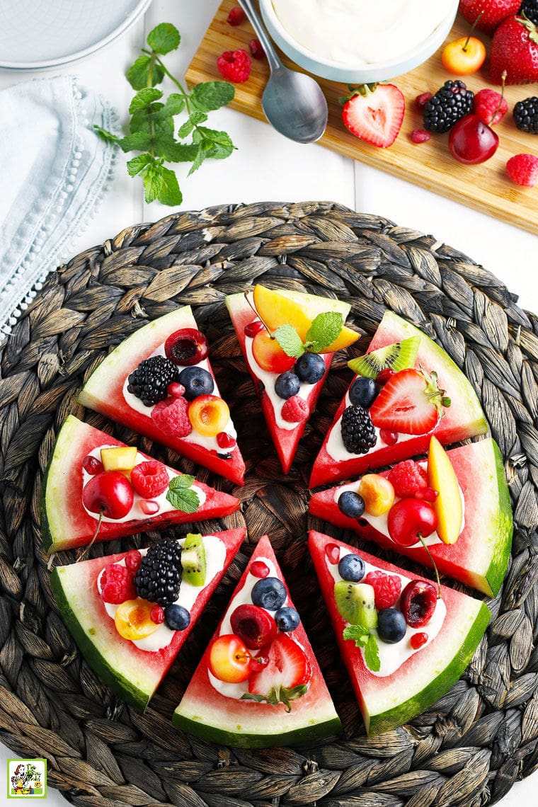 Slices of watermelon pizza with slices of fruit and berrieson a woven straw mat on a white tablecloth