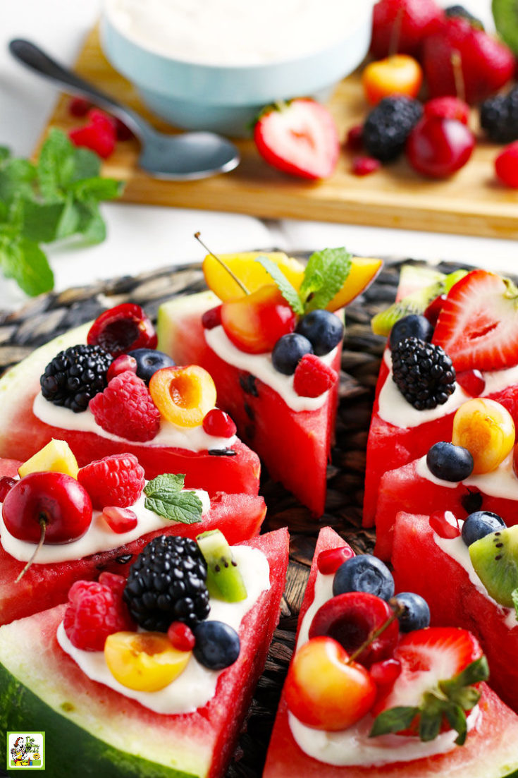 Closeup of slices of watermelon pizza with fruit and berrieson a woven straw mat with more fruit in the background