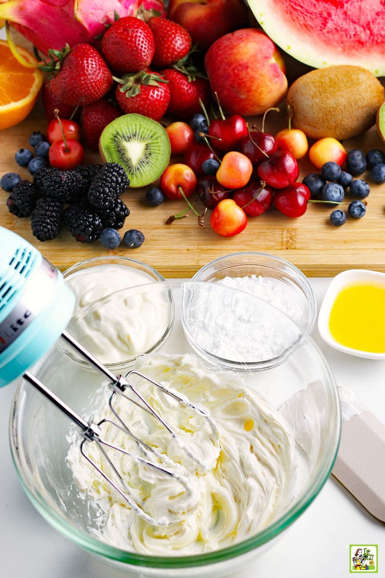 A hand mixer and ingredients for making cream cheese frosting plus fruit and berries for watermelon pizza