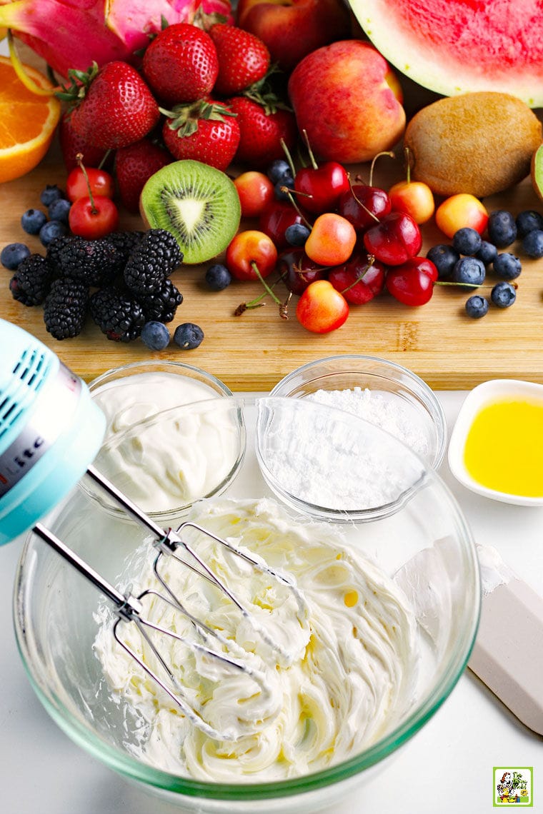 A hand mixer and ingredients for making cream cheese frosting plus fruit and berries for watermelon pizza